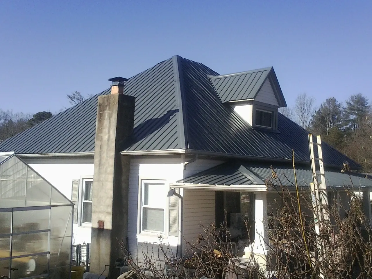 Dark blue standing seam metal roof on a white farmhouse with dormer — Slate & Tile Roof Repair by Roofing Brothers in Eagle Rock