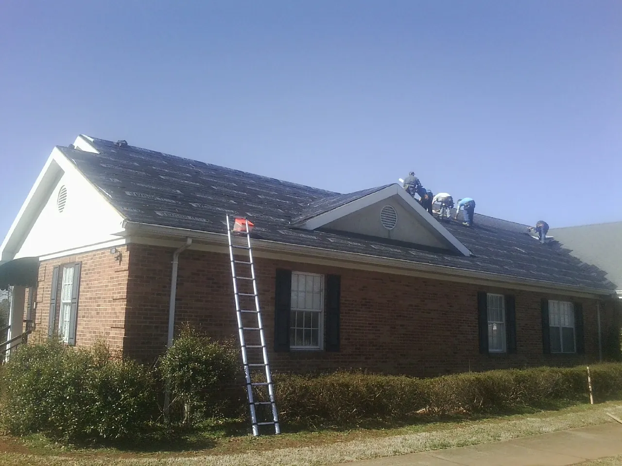 Crew tearing shingles off a brick ranch roof with a ladder set — Emergency Roof Repair work by our crew in Eagle Rock