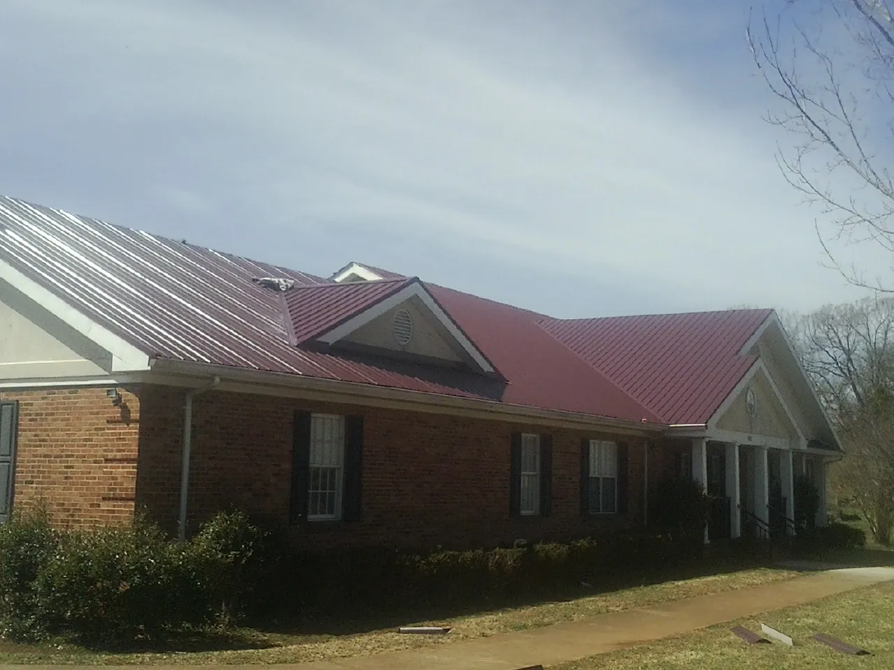 Red metal roof with gabled entries on a long brick building, from a Hail Damage Roof Repair job in Eagle Rock