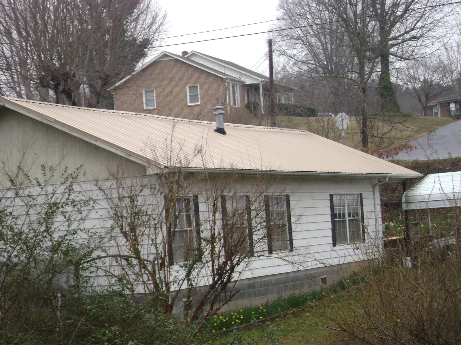 Tan metal roof on a white sided house set into a hillside — Commercial Roofing by Roofing Brothers in Eagle Rock